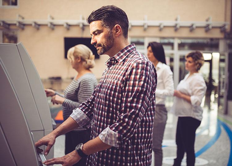 Man in a plaid shirt using an ATM.